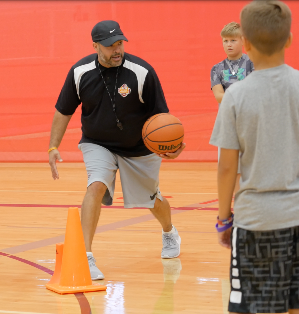 Coach Carlos holding a basketball and training two athletes at the Round Rock Sports Center. 