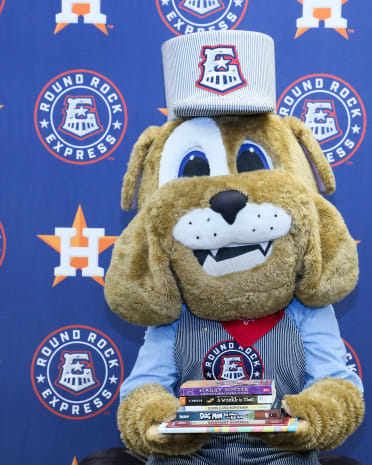 Spike, the Round Rock Express mascot, holding a pile of books. 