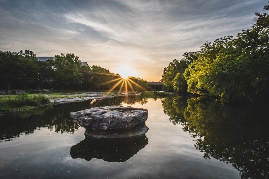 Round rock in middle of creek with sun rising in background