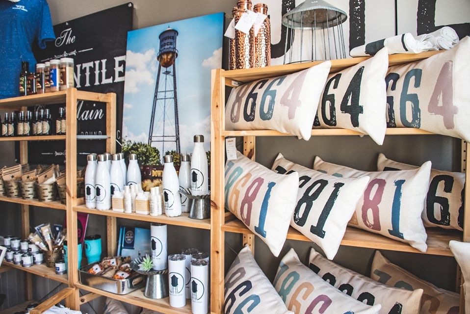Pillows, water bottles, candles on boutique product display shelf.