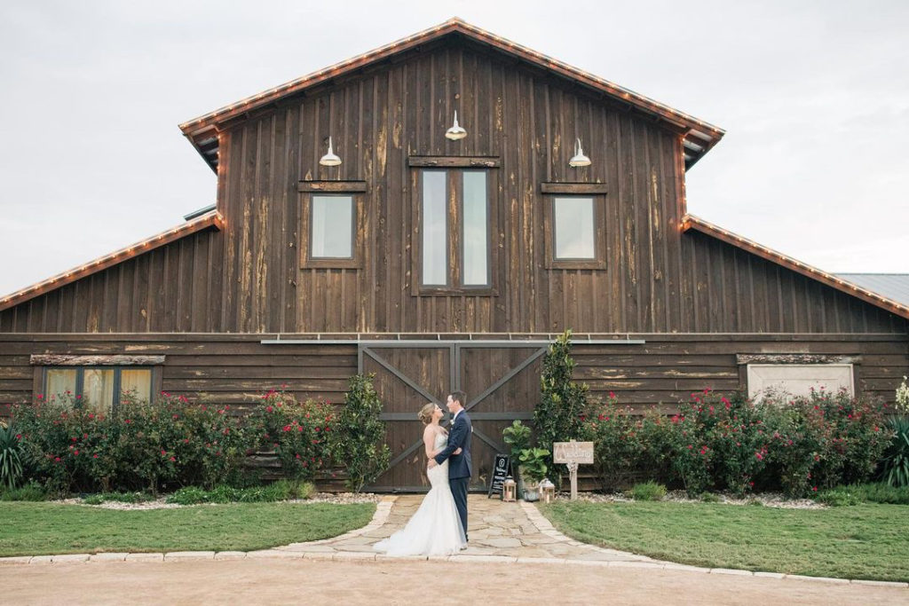 Bride and groom posing for  photo in-front of a barn.