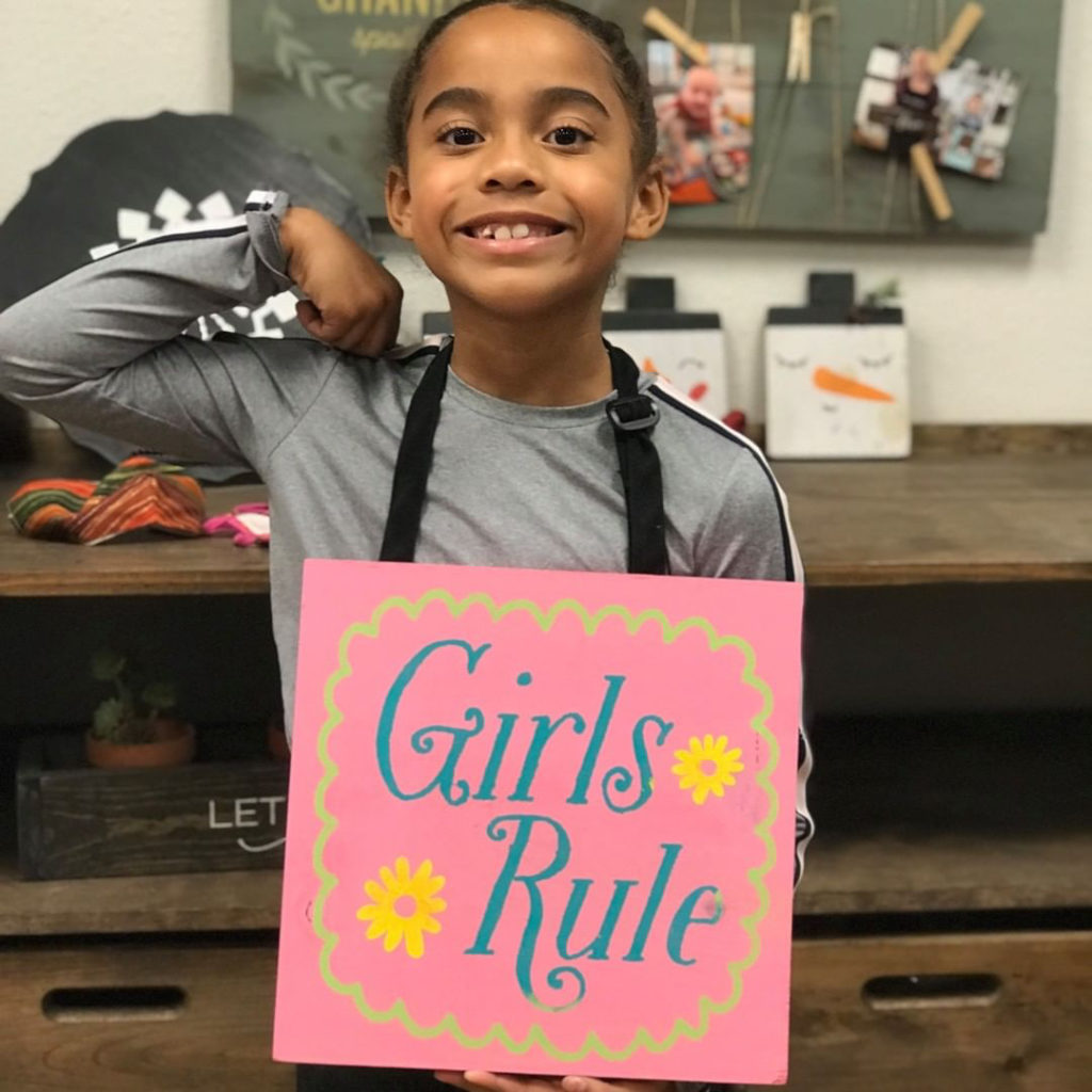 girl holding up artwork that says girls rule. 
