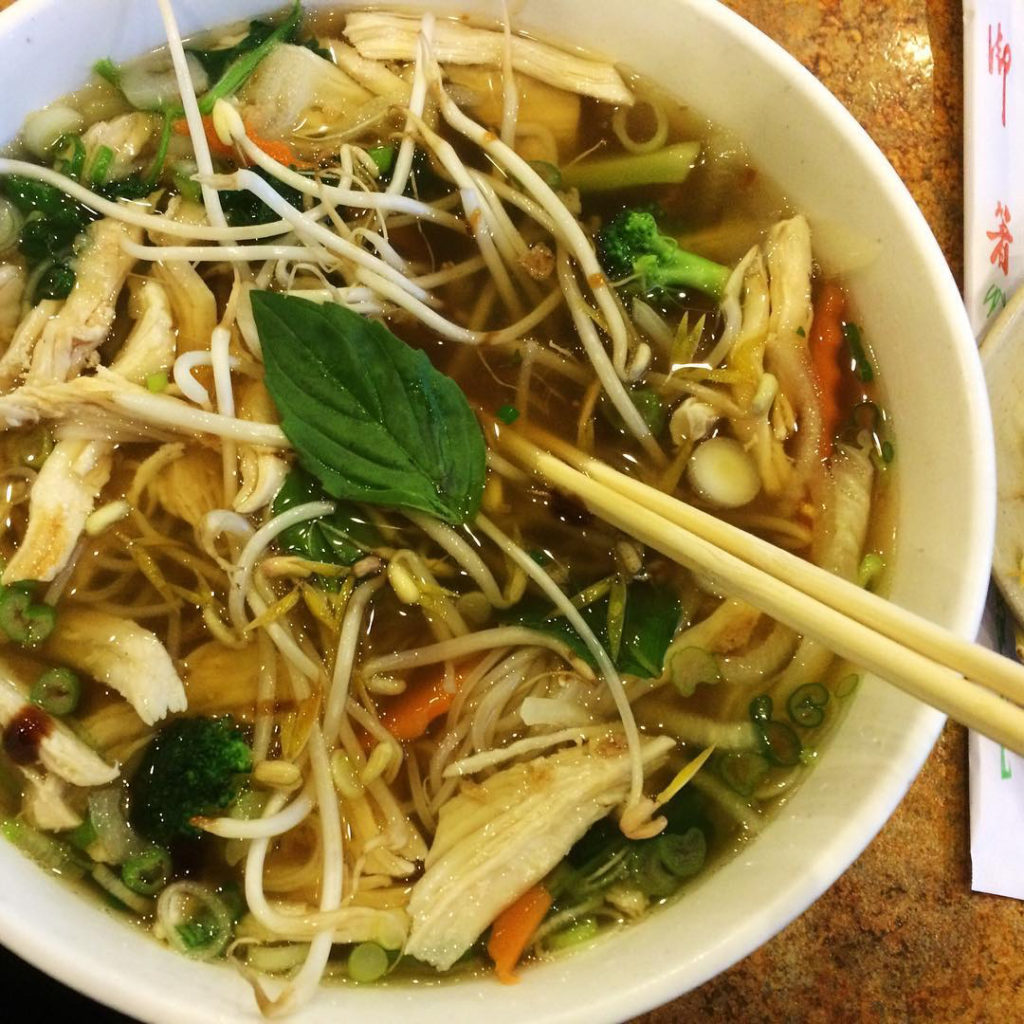 Photo of a bowl of pho with broth, noodles and chicken. 