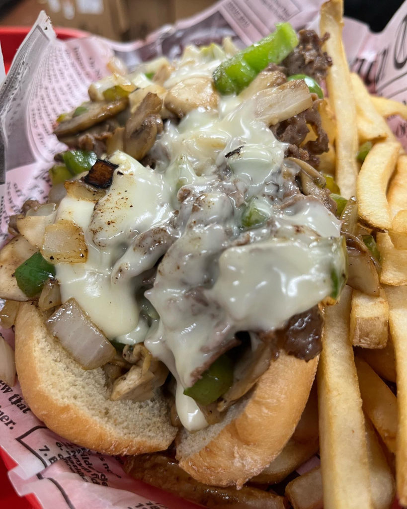 Picture of a Chicago cheesesteak with melted cheese. Fries on the side. 