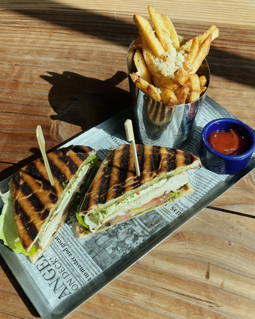 Picture of a pesto sandwich and fries on a wooden table. 