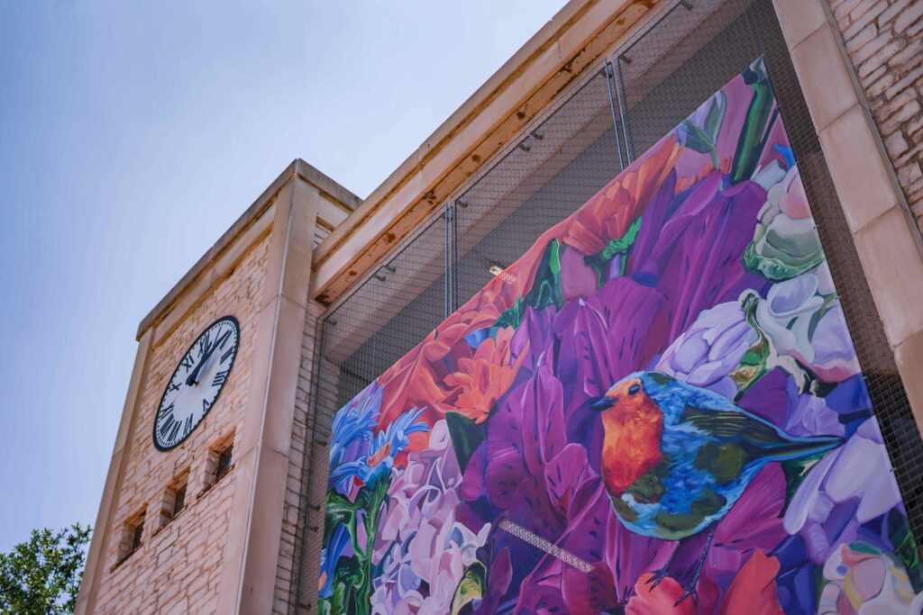 A colorful painting of a bird and flowers underneath a clock tower. 