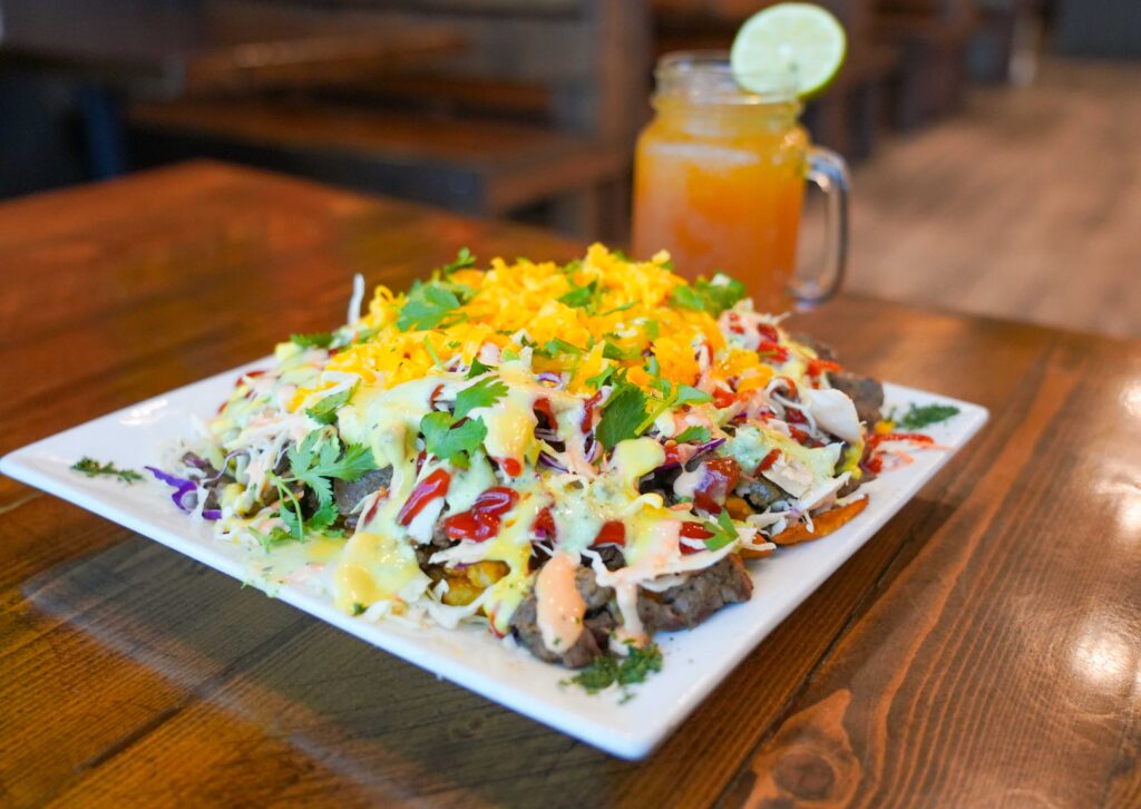 Loaded arepas topped with cheese, meat, and sauces at Arepitas, served with a drink.
