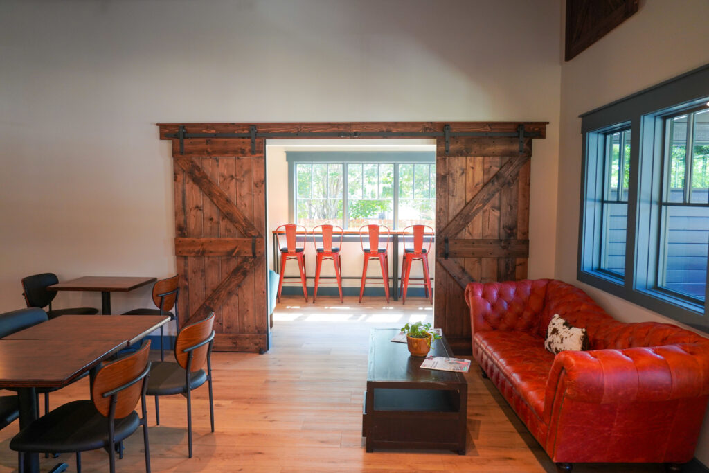 Interior of Purely Provisions with rustic barn doors, bright seating, and a red sofa.