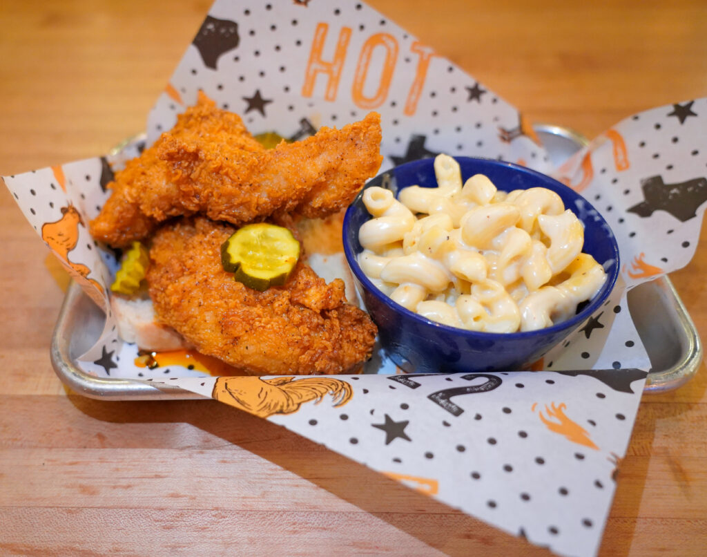 Tumble 22 hot chicken tenders with pickles served beside a bowl of macaroni and cheese.