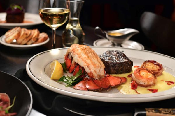 Steak and lobster plate with scallops, lemon, and glass of white wine.