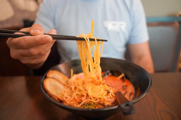 Person lifting ramen noodles with chopsticks over a bowl of soup.