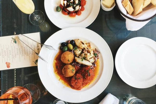 Flat-lay of Mediterranean dishes including falafel, olives, pita bread, and dips on a restaurant table.